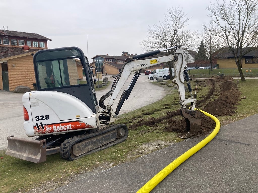 Bobcat compact excavator with yellow hose attachment on residential driveway during landscaping work