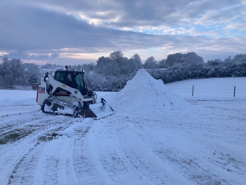 Compact snow removal machine pushing accumulated snow in a snowy field under cloudy skies